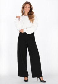Pulover alb tricotat cu mâneci lungi și largi; asortat cu pantaloni negri cu talie înaltă și tocuri negre cu vârful ascuțit.