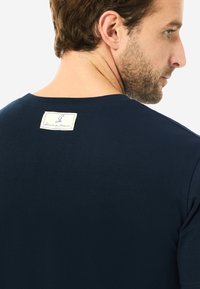 Marineblaues Kurzarm-T-Shirt aus Baumwolle, mit rundem Halsausschnitt und einem genähten Etikett auf der Rückseite mit Markendetails.