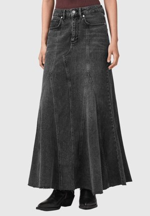 Longue jupe en jean noire avec des panneaux cousus et un ourlet brut, portée avec des bottines noires, montrée sur une personne de la taille aux pieds.