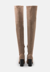 Beige Wildleder-Stiefel über dem Knie mit glatter Textur, ausgestattet mit einem Blockabsatz und einem Reißverschlussdetail auf der Rückseite.