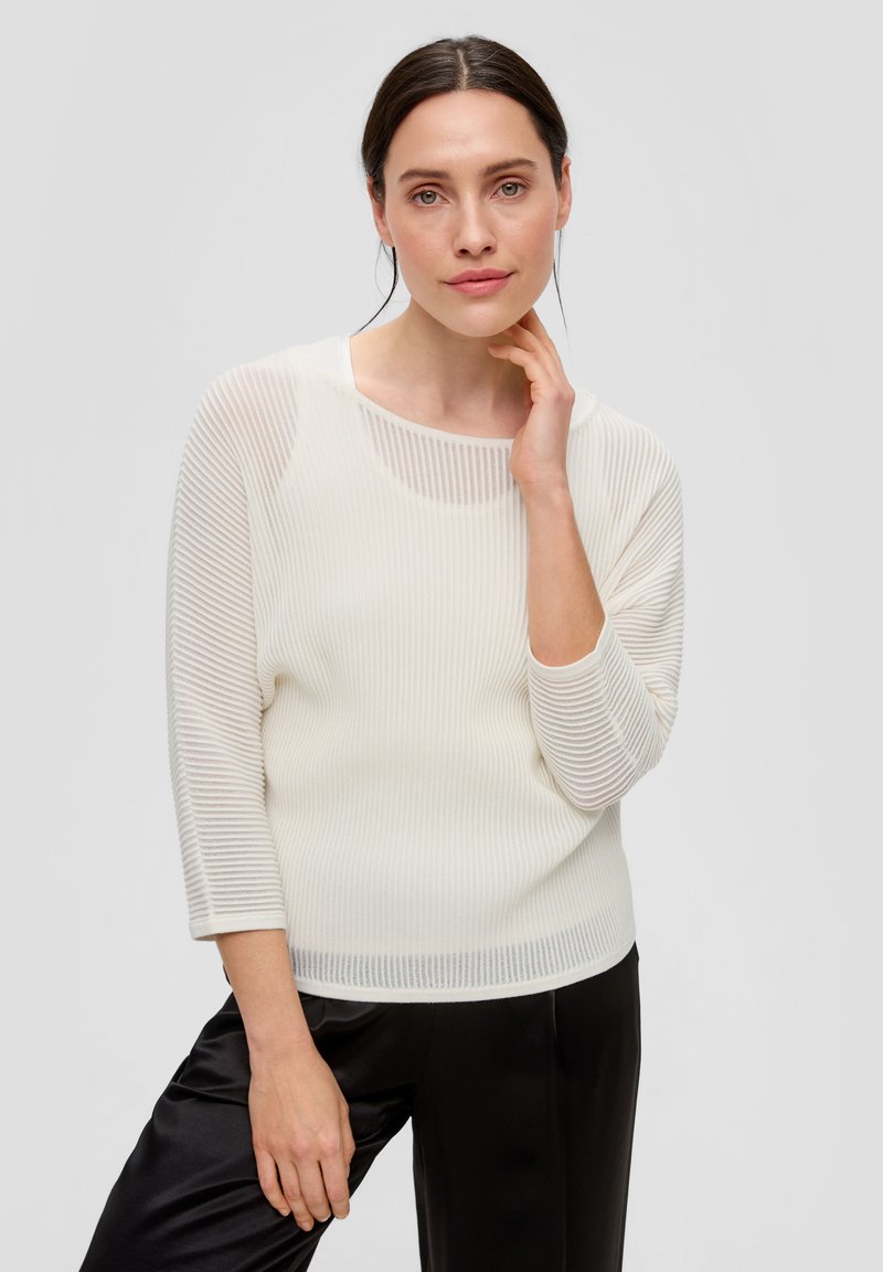 Weißer, gerippter Strickpullover mit Dreiviertelärmeln und weiter Rundhalsausschnitt. Kombiniert mit schwarzen Satinhosen, die ein leichtes und strukturiertes Design zeigen.