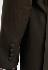 Manche de costume marron foncé avec quatre boutons noirs cousus en rangée près du poignet.