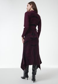 Vestido largo y ajustado en burdeos profundo con patrones geométricos negros. Hecho de punto texturizado, presenta un cuello alto y un dobladillo asimétrico.