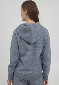 Grå hoodie med ett strukturerat mönster, som har en stor huva, ribbade ärmslut och nederkant. Tyget ser mjukt och bekvämt ut.