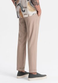 Pantaloni beige a sigaretta con orli arrotolati, abbinati a scarpe scivolate grigio scuro con un upper testurizzato e suole bianche.