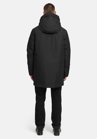 Melna, ar pūkām pildīta parka jaka ar lielu kapuci, kam ir taisna forma un garas piedurknes, apvienota ar melnām biksēm un zābakiem.