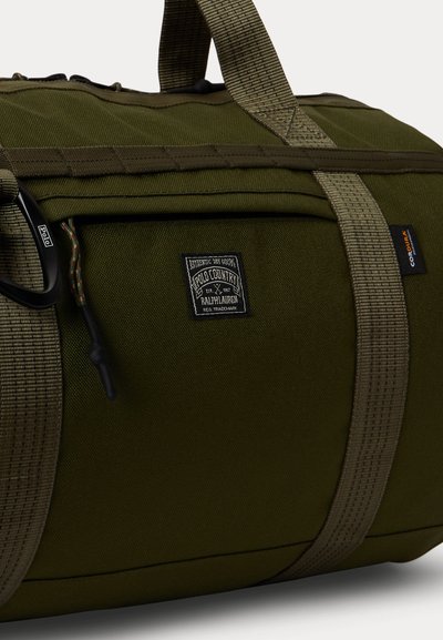 Τσάντα duffel σε ελιά πράσινο χρώμα με ανθεκτικούς ιμάντες, ταμπέλα Polo Country Ralph Lauren, μαύρο καραμπινέρ και ετικέτα από ύφασμα Cordura.