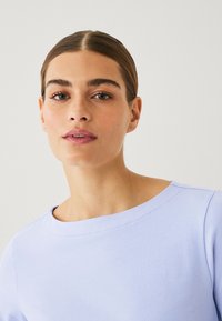 Lichtpaarse sweatshirt met een brede halslijn, gemaakt van zachte stof, met subtiele stikseldetails en een losse pasvorm.