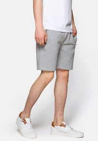 Szare bawełniane szorty z elastycznym paskiem i bocznymi kieszeniami, w połączeniu z białymi trampkami z brązowymi akcentami.