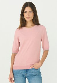 Ljusrosa kortärmad tröja med rund halsringning, ribbade ärmslut och avslut. Slät textur, figurnära design, kombineras med blå jeans.