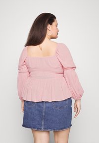 Top peplum rosa com mangas longas e bufantes e decote quadrado, tecido texturizado com padrões subtis, combinado com uma saia de denim azul.