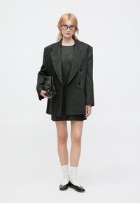 Szary dwurzędowy żakiet z szpiczastymi klapami na dopasowanej mini sukience. Noszony z białymi skarpetkami i czarnymi balerinami, trzymający fakturowaną czarną torebkę.