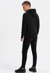 Felpa nera con tasca a marsupio e cappuccio con lacci, abbinata a jeans skinny neri strappati e scarpe da ginnastica nere.