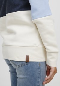 Fargeblokkerte sweatshirt med marineblå, lyseblå og kremfargede seksjoner. Mykt materiale med en beige lærlabel på kanten. Kombinert med denim.