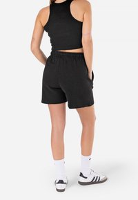 Černý žebrovaný tílko a černé šortky s pružným pasem. Model nosí bílé ponožky a černobílé tenisky. Čistý, jednoduchý design.