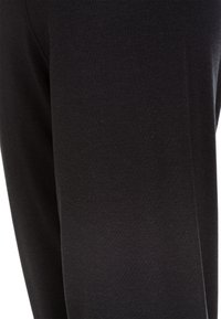 Leggings noirs en tissu doux et extensible, présentant une texture lisse et un design ajusté, avec des détails de couture visibles sur les côtés.