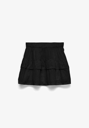 Minifalda negra de capas con cinturilla elástica y sutil textura de puntos sobre fondo blanco.