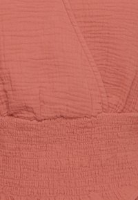 Indumento color corallo con un tessuto testurizzato e stropicciato. Presenta una smock arricciata in vita e un design avvolgente.