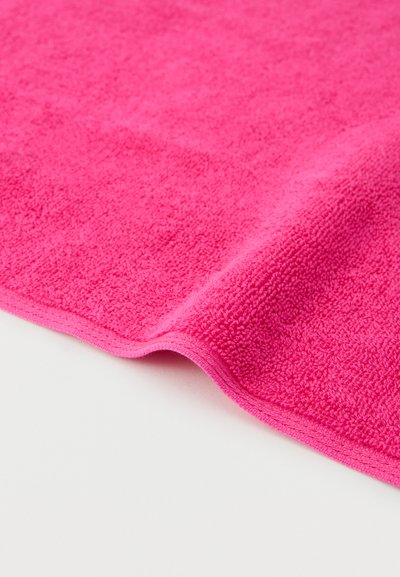 Φωτεινή ροζ πετσέτα από περκάλι με διπλωμένη άκρη πάνω σε λευκή επιφάνεια, τονίζοντας το μαλακό, υφασμάτινο ύφασμά της.