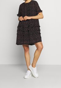 Czarna sukienka z drobnym różowym kwiatowym wzorem, z falbanami na kilku warstwach, krótkimi rękawami i białymi trampkami. Gładka faktura, styl casualowy.