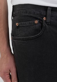 Schwarze Jeans aus Denim mit kupferfarbenen Beschlägen, ausgestattet mit einer Vorderentasche, schlankem Design und subtiler Textur. Maßgeschneiderte Passform mit klassischer Naht.