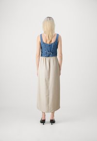 Denim overdel med tank-stropper, indsnævret talje, beige maxinederdel. Har en bageste spænde detalje og sorte hælede klipklappere. Glat tekstur.