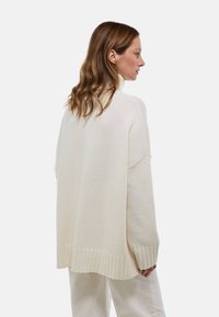 Pull crème surdimensionné en tricot doux, avec un ourlet et des poignets côtelés, un col montant et des épaules tombantes.