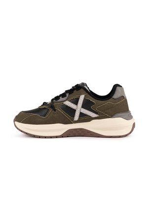 Vista laterale di una sneaker verde oliva e nera con dettaglio bianco testurizzato "X" e suola spessa bianca e marrone.