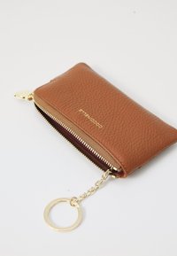 Portafoglio in pelle marrone con finitura texture, zip dorata e anello portachiavi. Caratterizzato da un interno bordeaux e una forma rettangolare compatta.