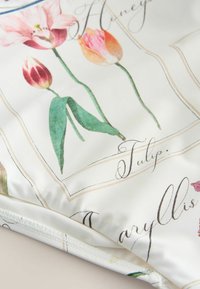Gros plan sur un tissu avec des illustrations de tulipes et de callas, étiquetées avec des noms de fleurs en écriture cursive sur fond blanc.