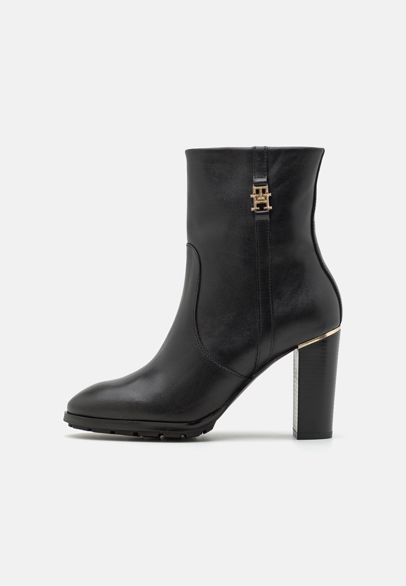 Bottine en cuir noir avec un bout pointu, des détails métalliques dorés et un talon bloc haut avec un design texturé. Texture lisse sur toute la surface.