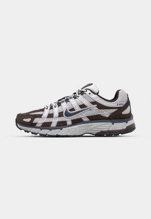 Chaussures de sport brun et blanc avec des panneaux en maille, des accents réfléchissants et des semelles texturées. Elles disposent d'un système de laçage pour un ajustement sécurisé.