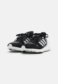 Czarne buty sportowe z teksturowaną cholewką z dzianiny, trzema białymi paskami i białą podeszwą z zielonymi akcentami oraz wzorzystym noskiem.