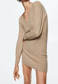 Robe en maille côtelée beige avec un décolleté en V profond, des manches longues et une silhouette ajustée. Texture douce et détail d'ourlet légèrement asymétrique.