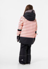 Rot-weiße gestreifte isolierte Jacke mit einer schwarzen Kapuze, kombiniert mit schwarzen Schneehosen mit reflektierenden Akzenten und einem Logo.