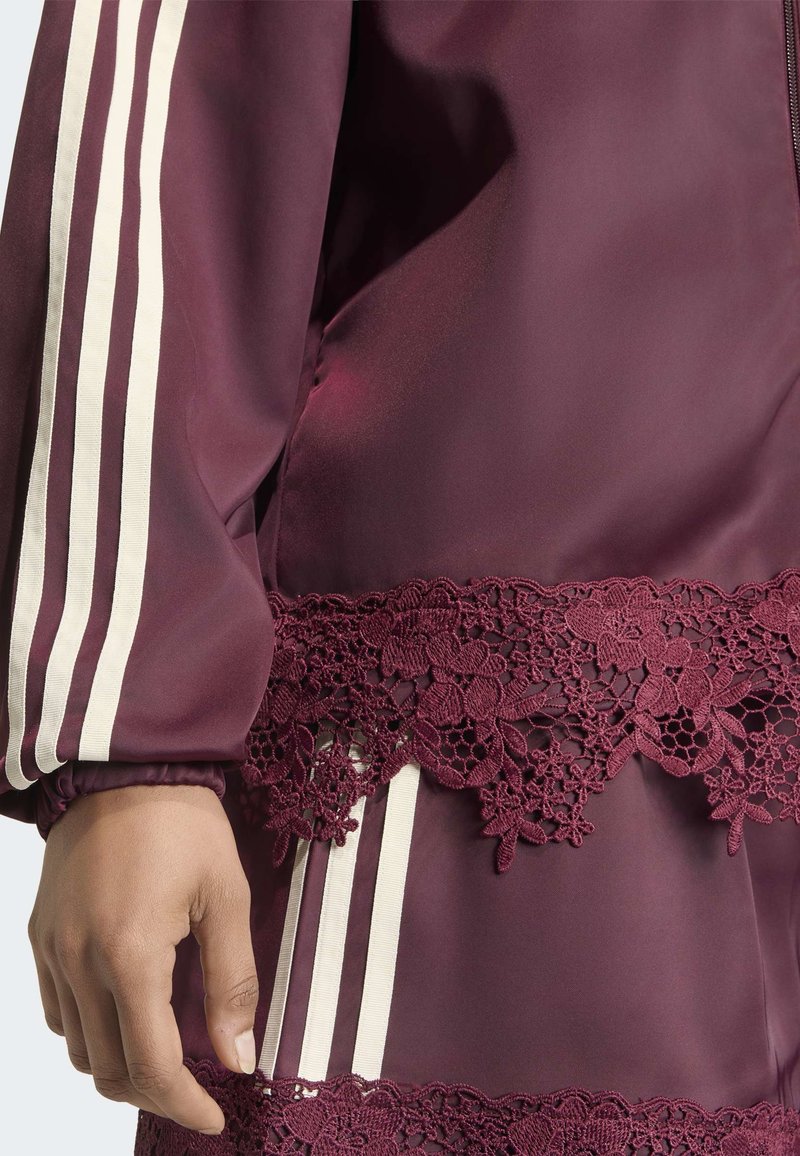 Main reposant à côté d'un vêtement en satin bordeaux avec des rayures blanches et une bordure en dentelle florale sur la manche et la taille.