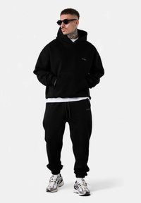 Ensemble de sweat à capuche noir et de pantalon de survêtement, avec un ajustement décontracté, une poche kangourou et un logo assorti. Assorti avec des baskets réfléchissantes.