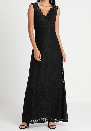 Sleeveless black lace gown with scalloped V-neckline and floor-length hem, worn with black open-toe heels on a plain white background.