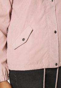 Ljusrosa jacka med en avslappnad passform, som har elastiska ärmslut, en sidficka med tryckknapp och justerbar dragsko i nederkanten.