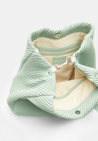  világoszöld, texturált táska bordázott külső résszel, puha bélésű, patentos záródással és belső cipzáras zsebbel. Az alakja laza és hétköznapi.
