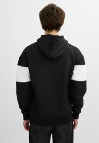 Sudadera negra con tejido texturizado, paneles en los hombros blancos y capucha con cordón. El diseño incluye puños y dobladillo con canalé.