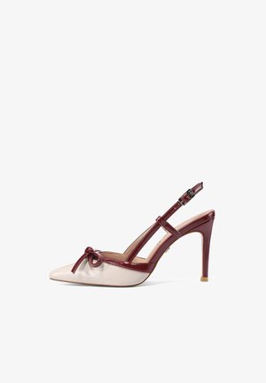 Zapato de tacón alto beige de punta puntiaguda con ribete de charol granate, detalle de lazo en la punta y hebilla ajustable en la correa del tobillo.