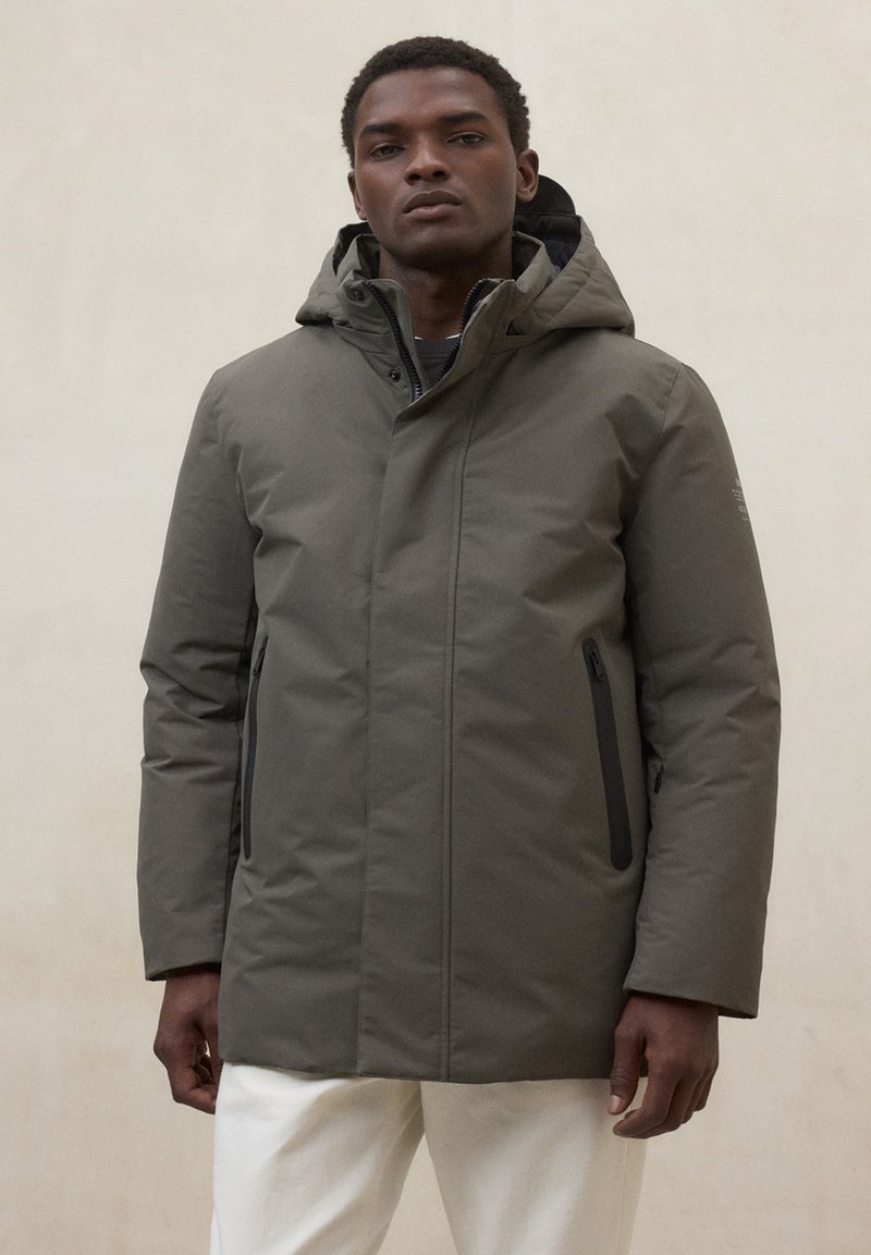 Parka imbottito verde con cappuccio, cerniera frontale e due tasche laterali con cerniere nere. Texture liscia e design minimalista.