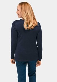 Marineblauwe longsleeve top met een geribbeld textuur, ronde halslijn en een zoom die iets langer is aan de achterkant, gecombineerd met donkerblauwe jeans.