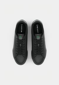 Baskets en cuir noir avec une finition lisse, dotées d'un bout arrondi, de lacets plats et d'une étiquette logo verte sur la languette.