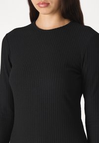 Black ribbed long-sleeve top featuring a round neckline, form-fitting silhouette, and smooth texture, with vertical stripes enhancing the design.