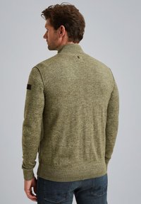 Oliven grøn sweater med høj krave, ribbede manchetter og kant. Den har et struktureret strik og et lille logo på venstre ærme.