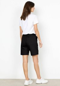 Svarta shorts med elastisk midja, sidfickor och en enkel design. Matchas med en enfärgad vit t-shirt och vita sneakers.