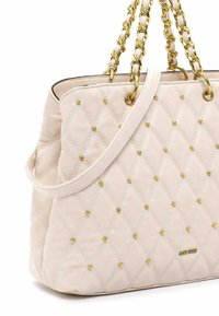 Borsa a tracolla trapuntata beige con borchie dorate, manici doppi in catena dorata e una forma strutturata. Texture liscia con dettagli eleganti.