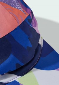 Multicolored cap featuring geometric patterns in shades of pink, blue, and purple. Made of smooth fabric with contrasting stitching details.